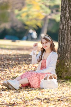 A young woman enjoying a sunny day in a park, dressed in a red dress and white cardigan.
