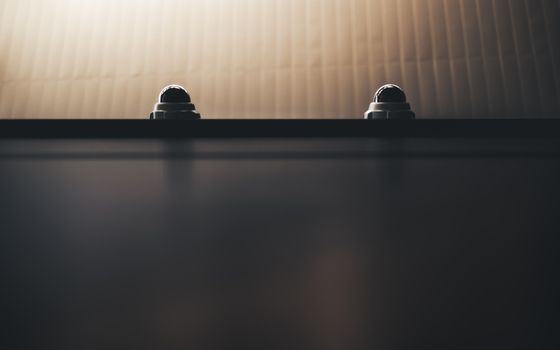 Two dome security cameras on a wall in dim lighting, emphasizing surveillance.