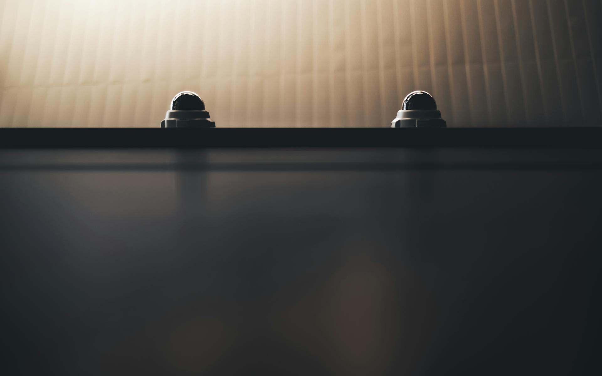 Two dome security cameras on a wall in dim lighting, emphasizing surveillance.