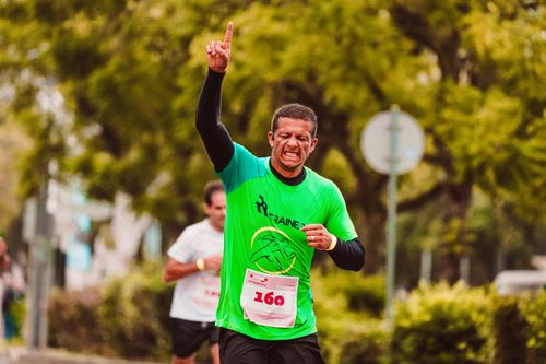 Free Joyful male runner celebrates a marathon win outdoors, raising arms in triumph. Stock Photo