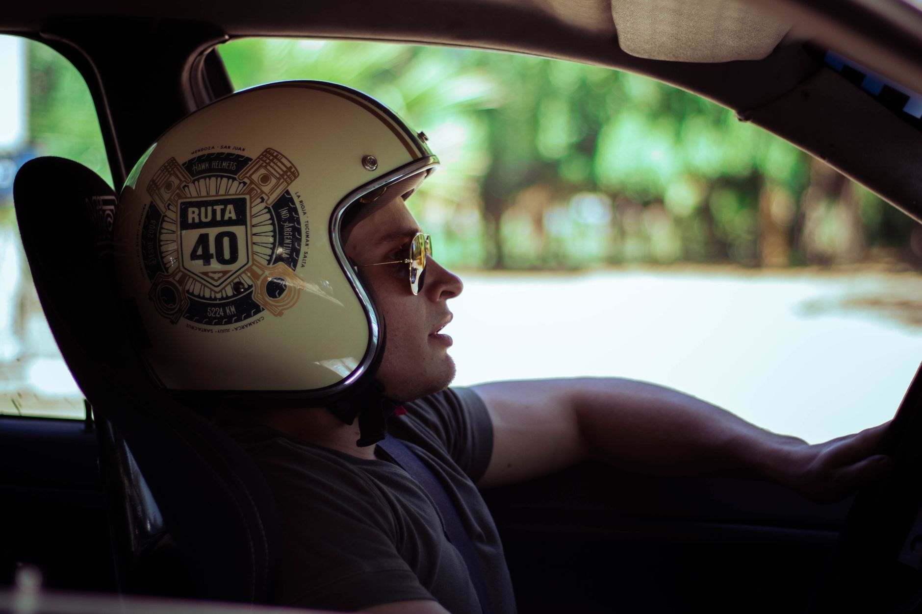 Man wearing a Ruta 40 helmet driving a car, looking into the distance.
