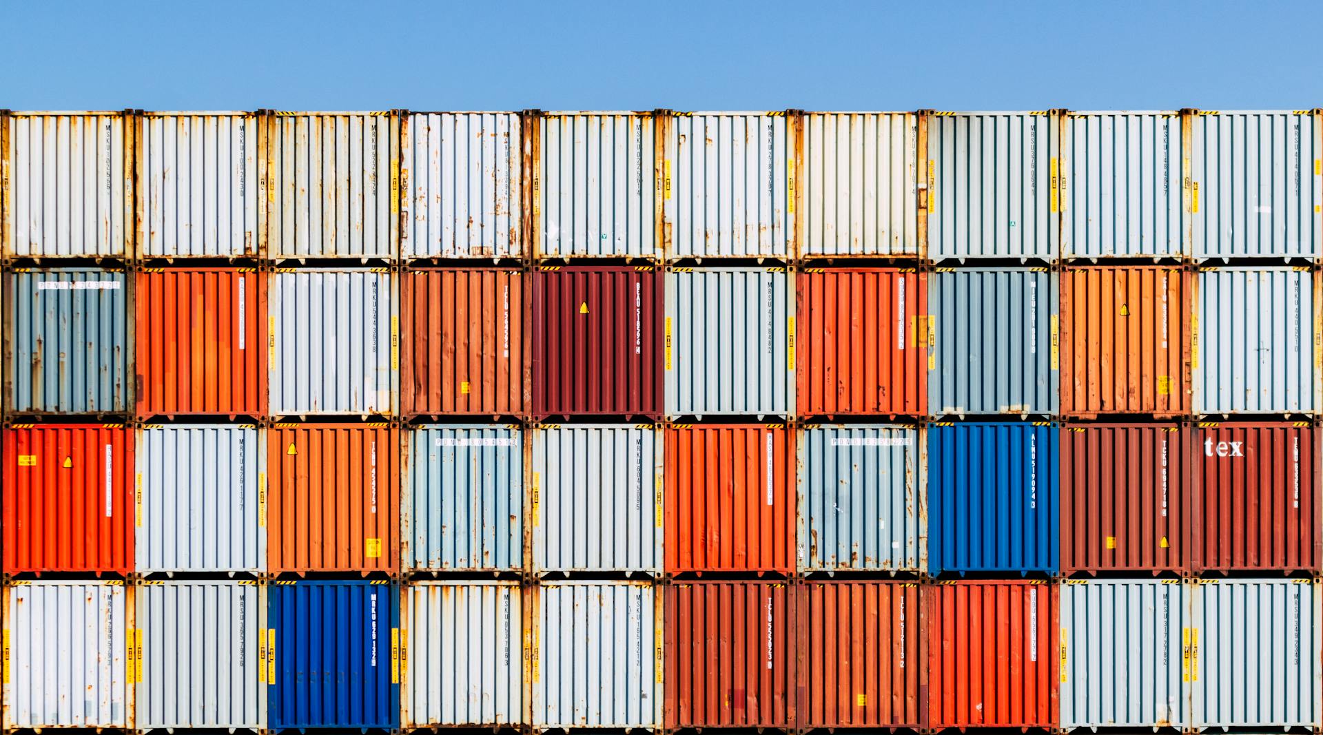 Colorful stacked shipping containers against a vibrant blue sky, conveying global trade and logistics.