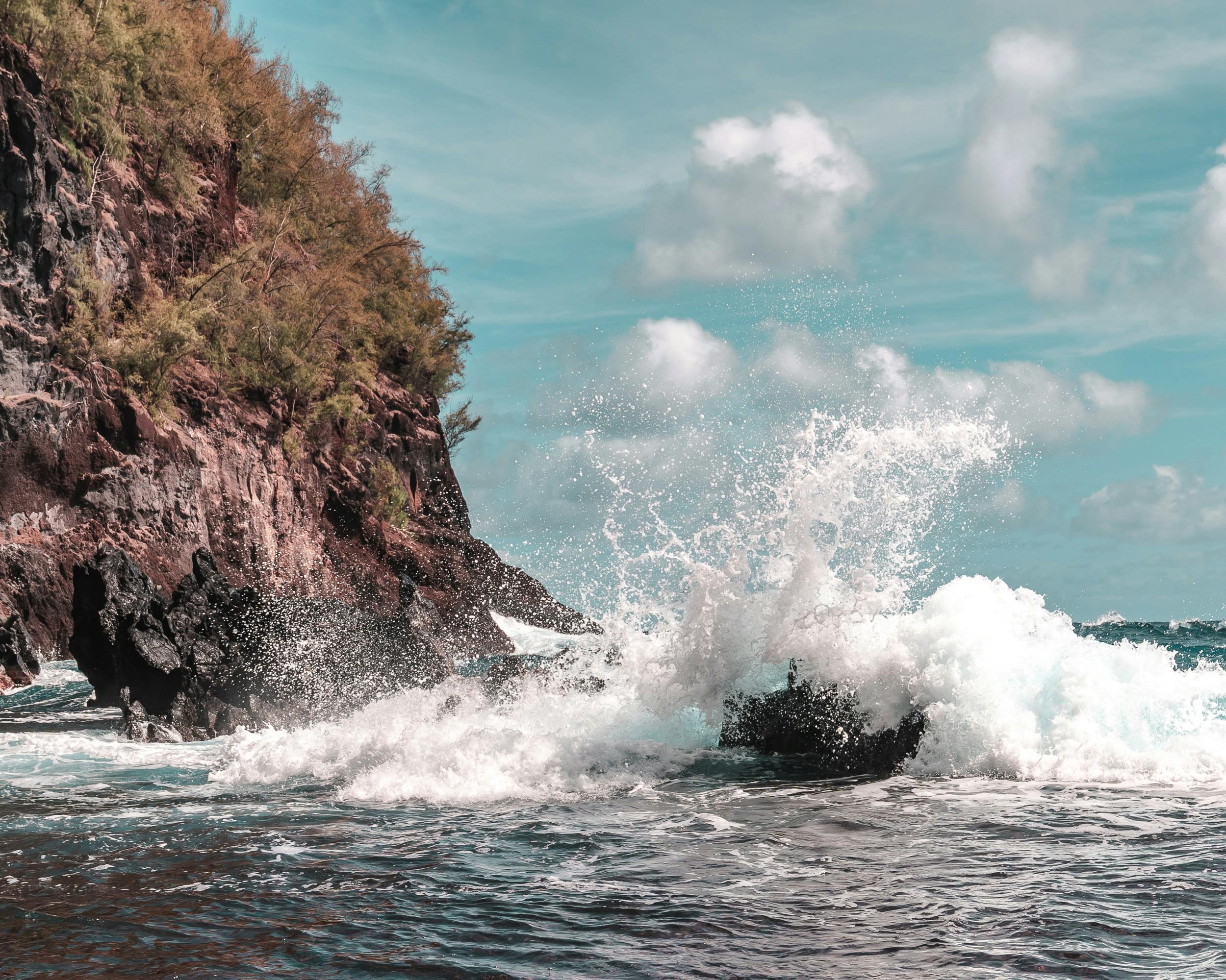 Waves crash against rocky cliffs under a vibrant blue sky. Perfect for nature and travel imagery.