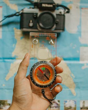 Close-up of a hand holding a compass over a map with a camera in the background. Ideal for navigation and travel themes.