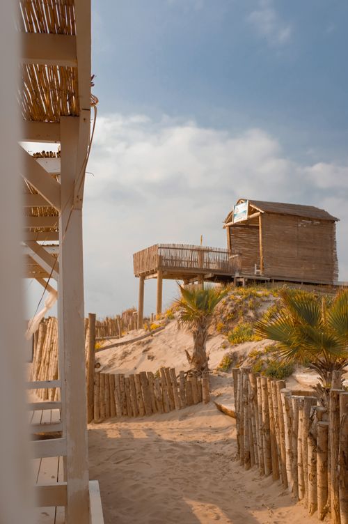 Free A wooden beach hut on sandy dunes against a clear blue sky, with wooden fencing. Stock Photo
