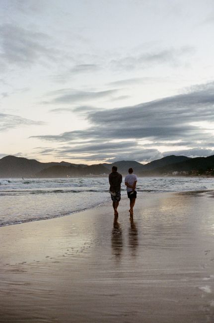 Two men walk along Santinho Beach, Florianópolis at sunset, capturing a serene moment by the sea.