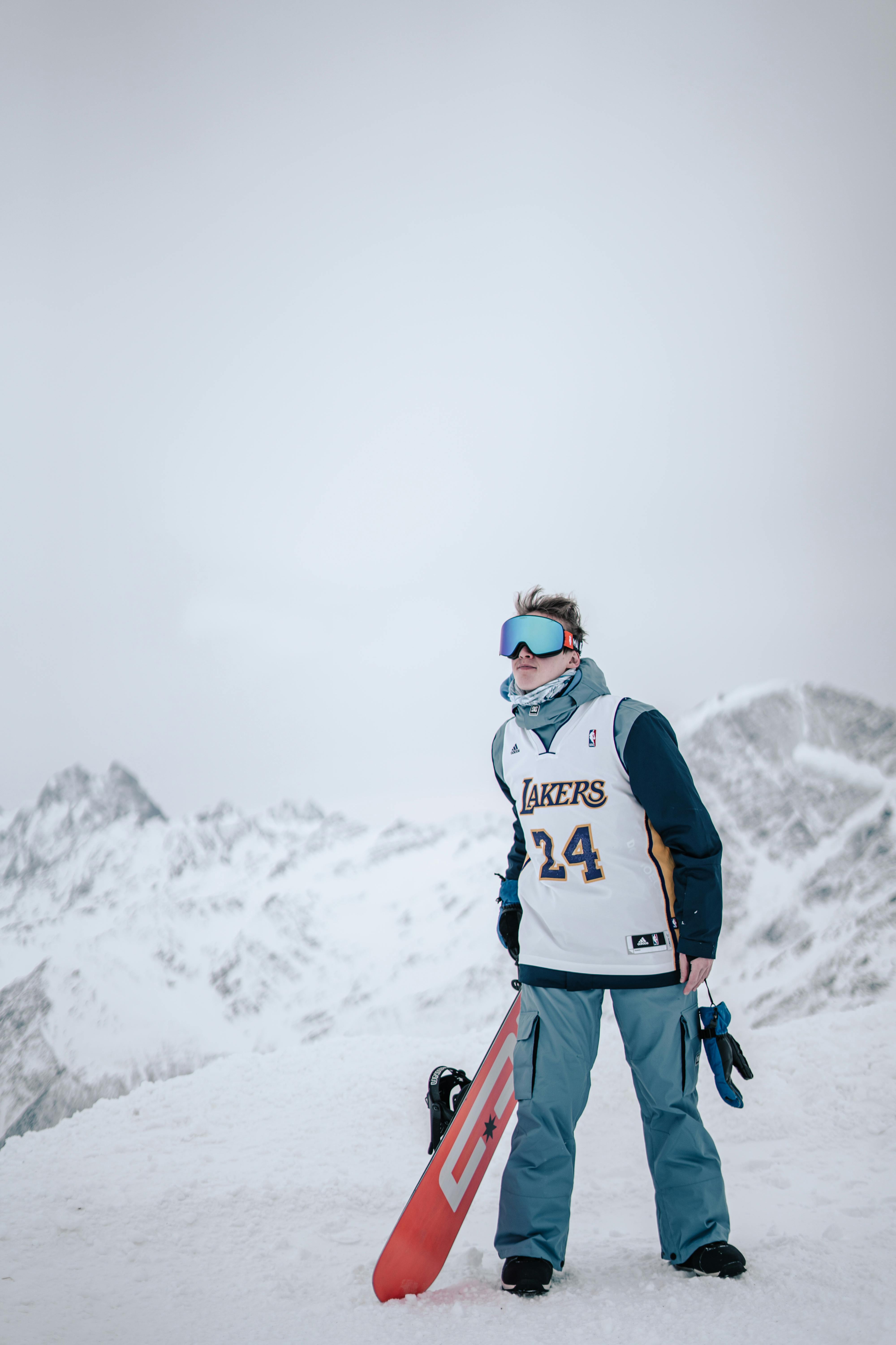 Prescription Goggle Inserts - Snowboarder wearing Lakers jersey stands atop a snowy mountain, ready for adventure.