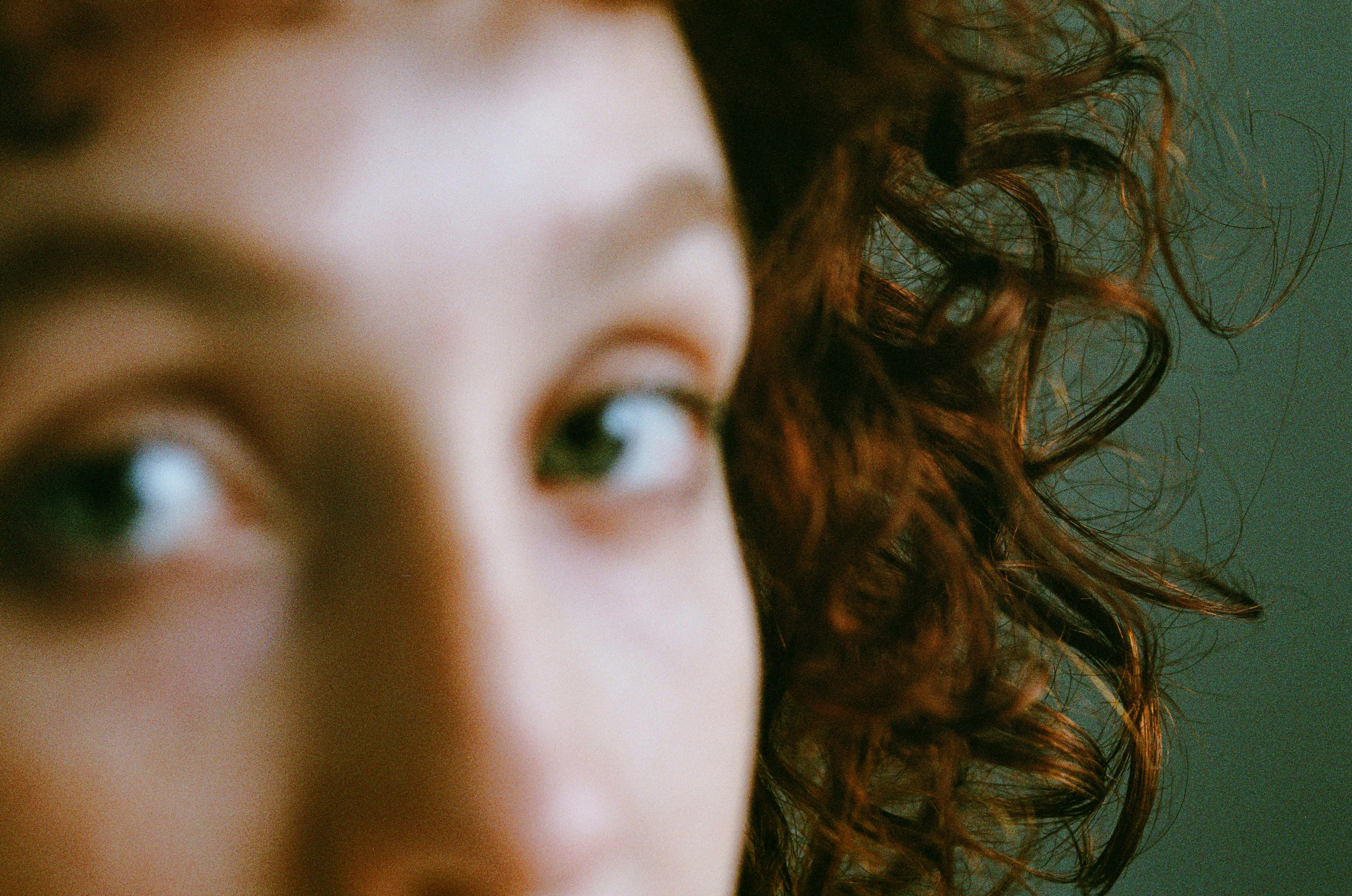 Blurred close-up of a woman's face featuring curly hair and eyes, with a focus on artistic expression.