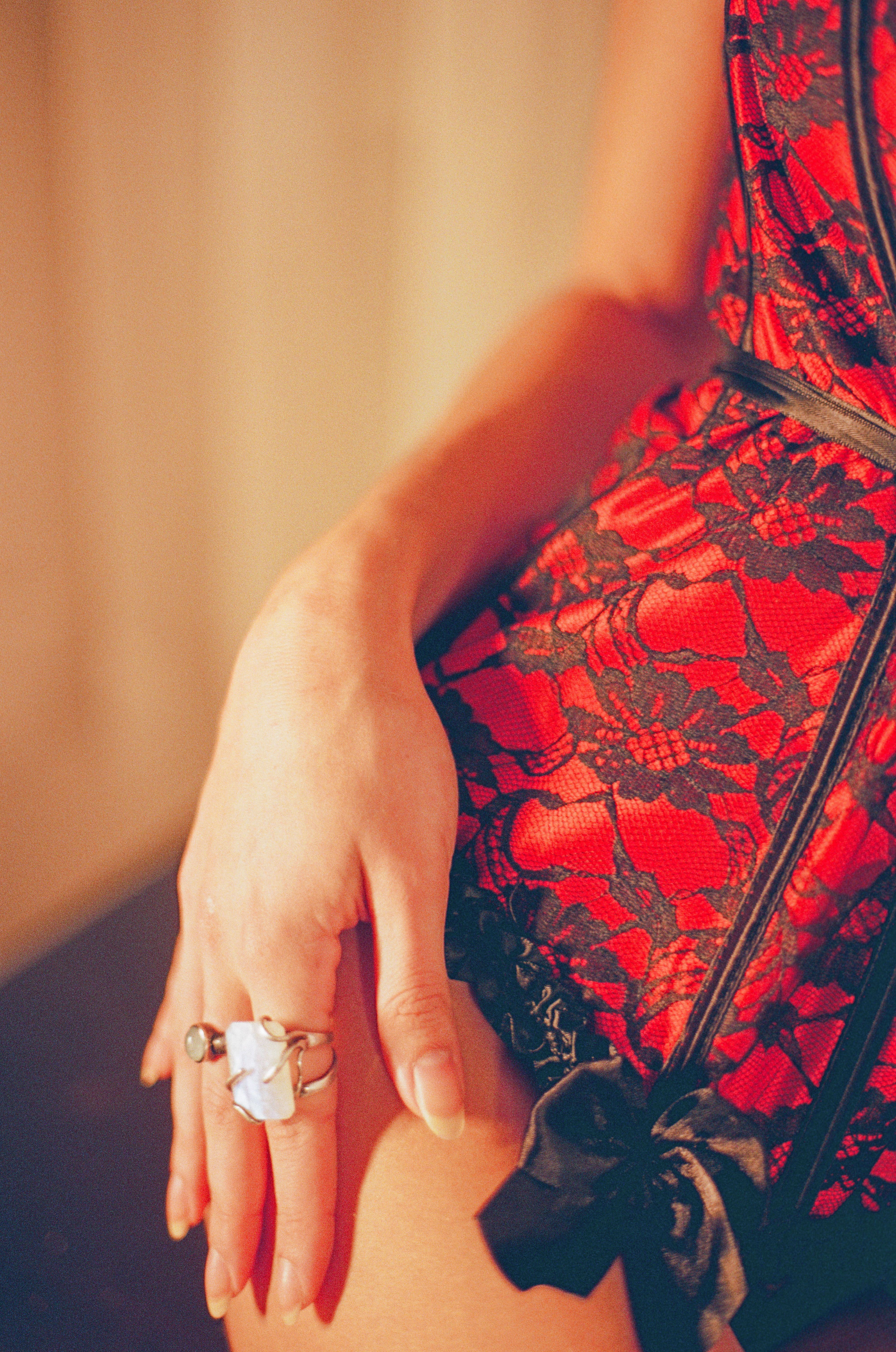 A close-up of a hand adorned with rings resting on red lace lingerie, capturing elegance and sensuality.