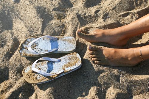 Free Close-up of sandy feet and flip flops on a beach in summer, evoking relaxation and vacation vibes. Stock Photo