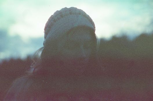 Silhouetted portrait of a woman in a beanie, blurred outdoors with soft ambient light.
