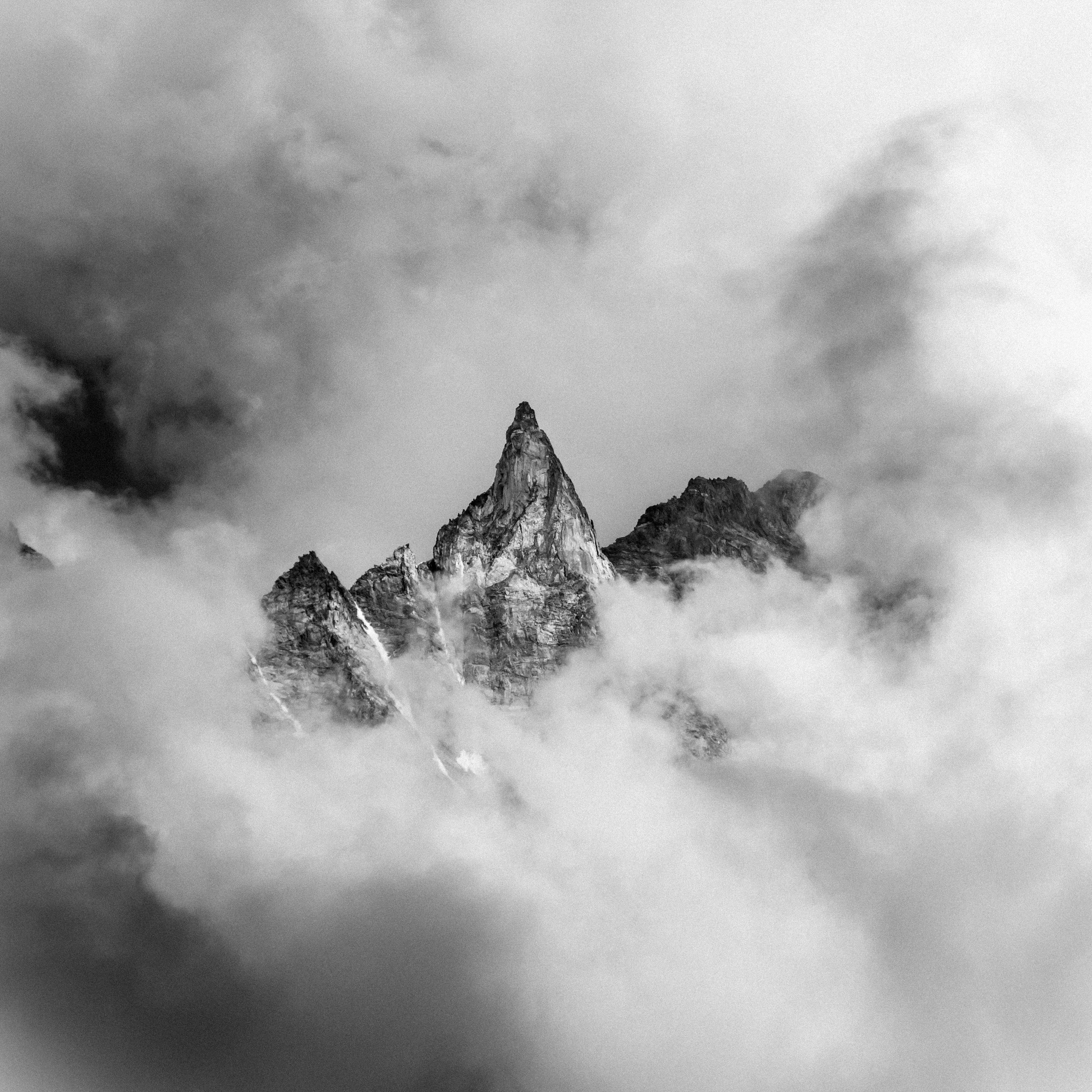Black and white photo of rugged mountain peaks surrounded by misty clouds, creating a moody landscape.