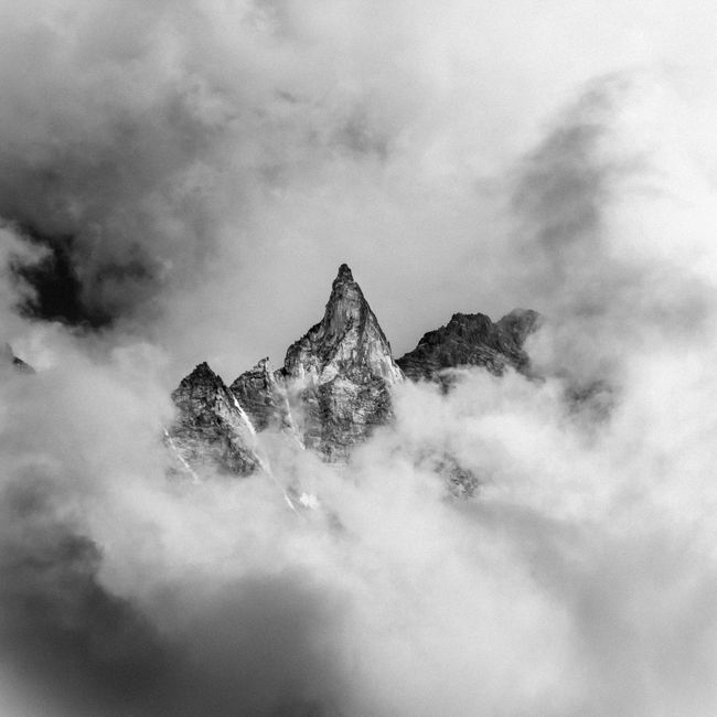 Black and white photo of rugged mountain peaks surrounded by misty clouds, creating a moody landscape.