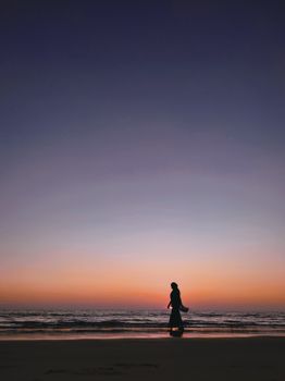 A serene silhouette of a person walking along a beach during twilight in Bangladesh.