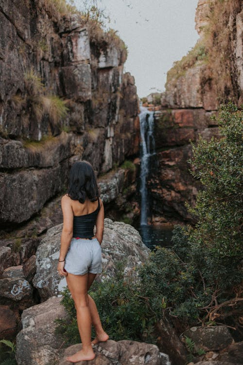 Free Woman Standing on a Rock Looking at a Waterfalls Stock Photo