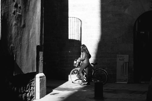 Free Black and white photo of a woman with a bicycle in a shadowy urban street. Stock Photo