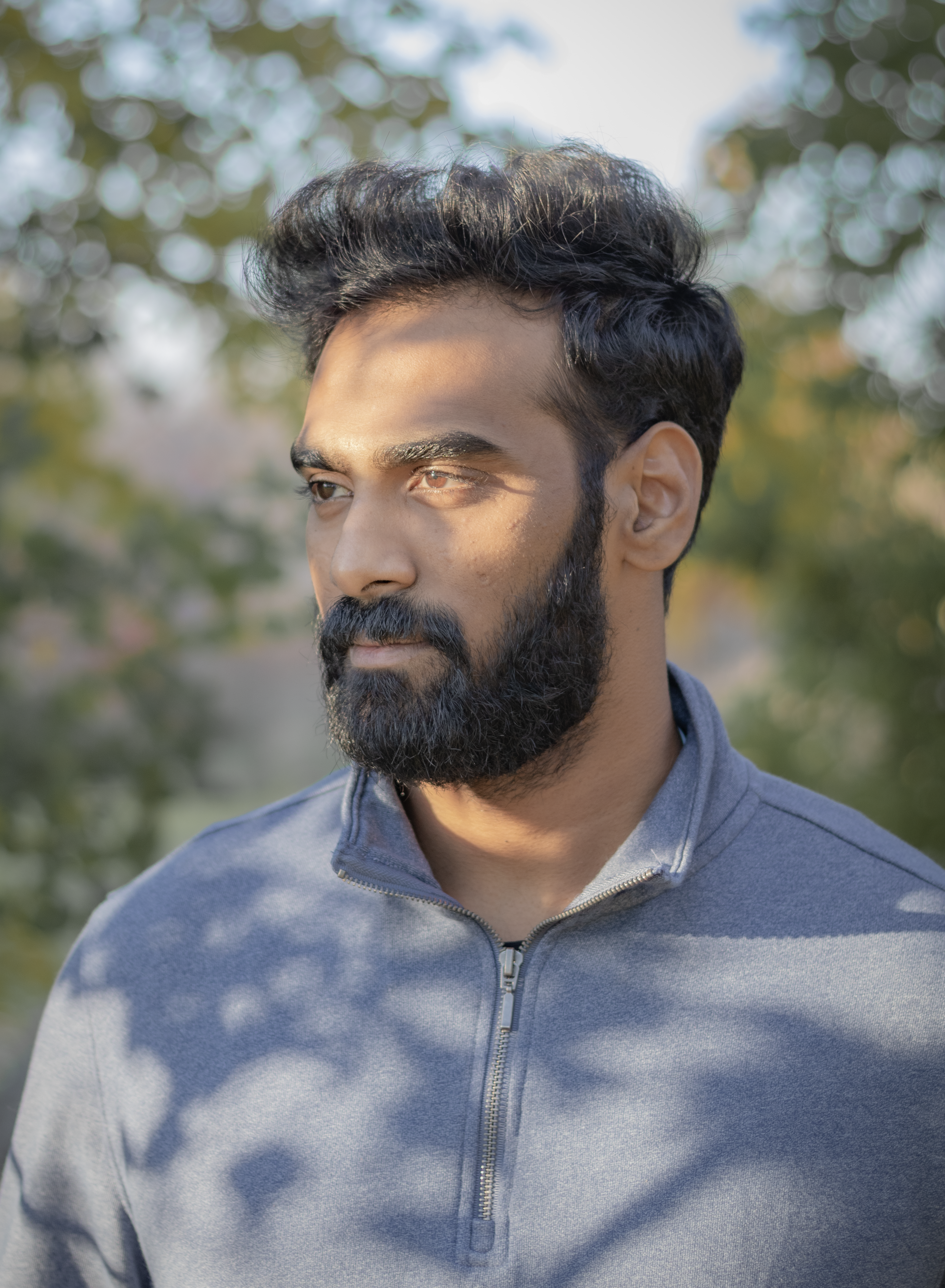 Close-up of a bearded man wearing a grey jacket outdoors in natural light.