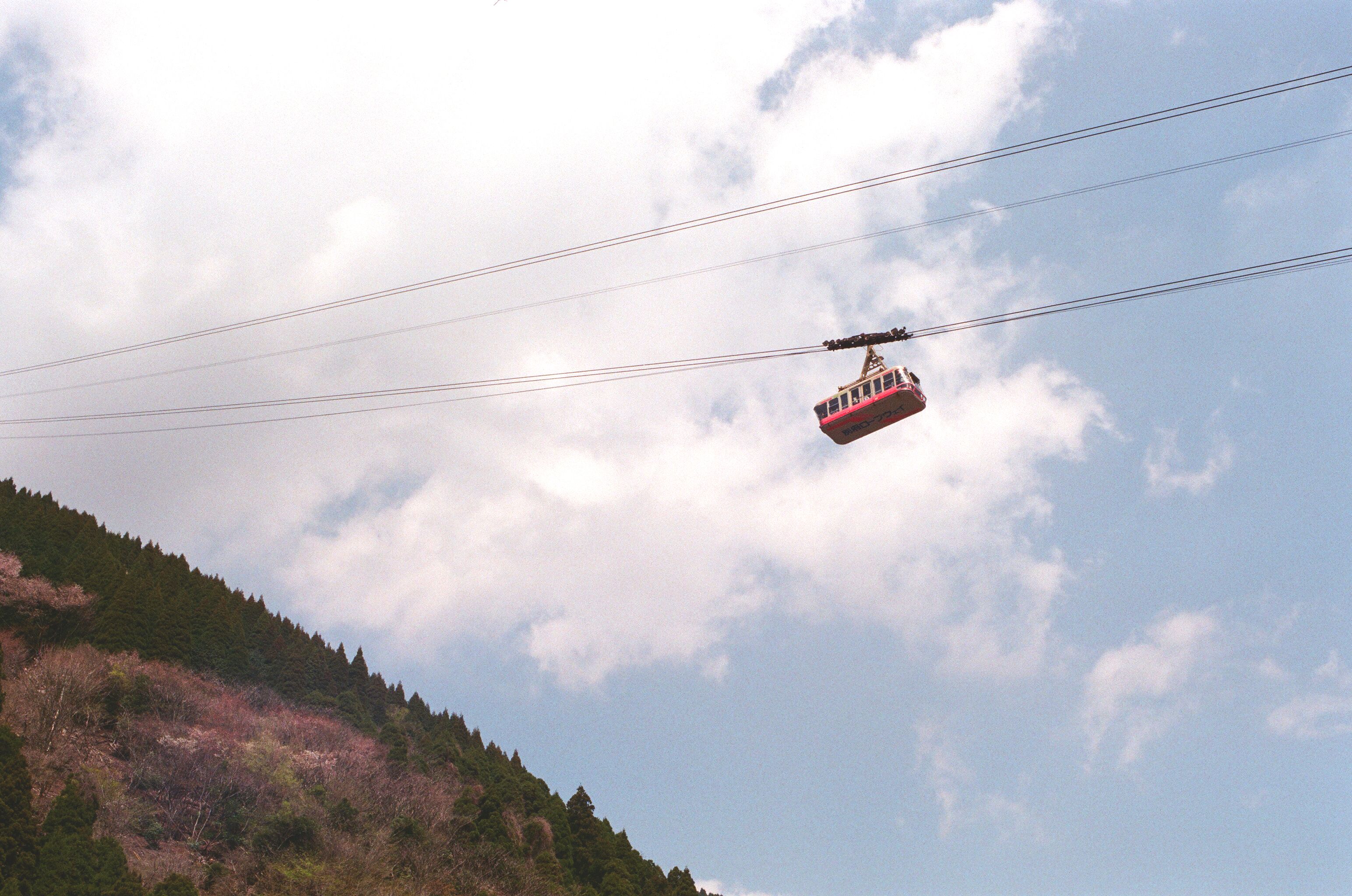 Red cable car traveling over mountains on a bright day with fluffy clouds.