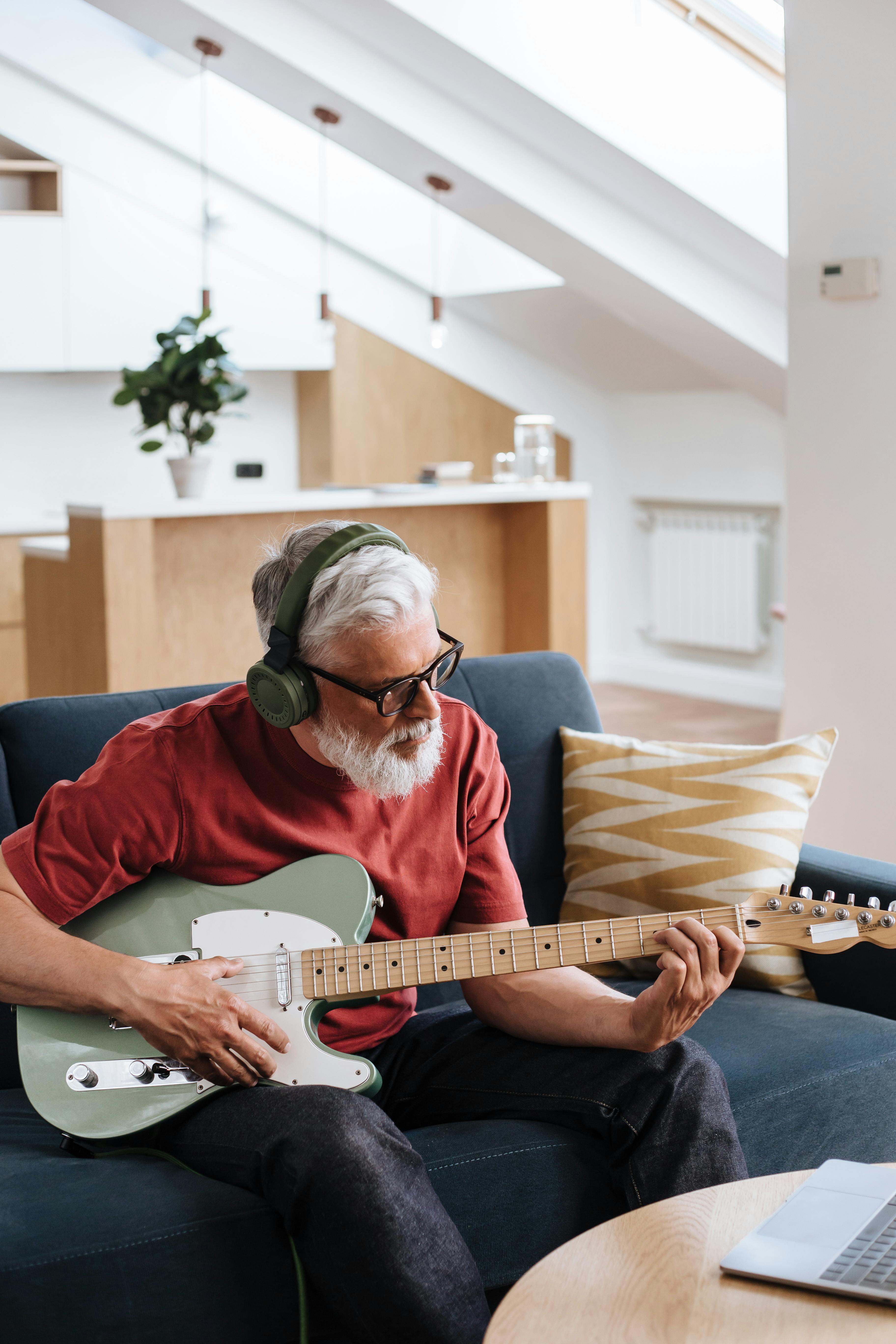 Senior man with headphones playing guitar in modern living room setting.
