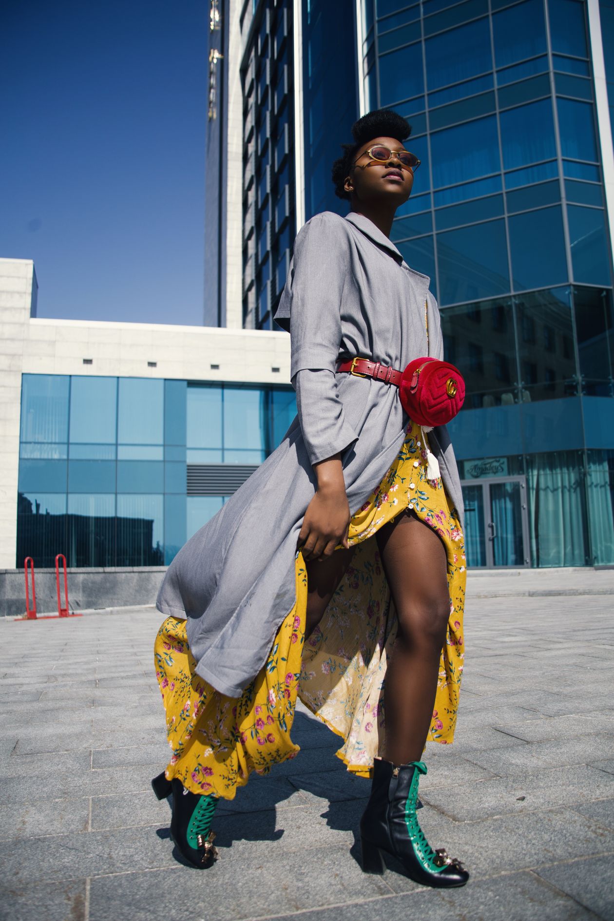 Woman layering a yellow floral midi dress with a long gray coat and boots