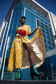 A fashionable woman in a floral yellow dress poses confidently in front of a modern glass building.