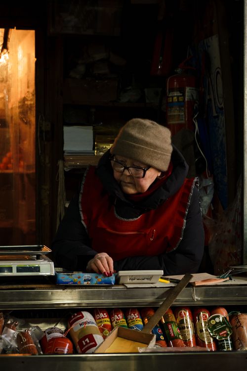 Free An elderly woman in warm clothing selling products at a local market stall. Stock Photo