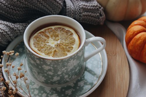 Free Warm autumn scene featuring citrus tea in a floral cup surrounded by pumpkins and a knitted scarf. Stock Photo