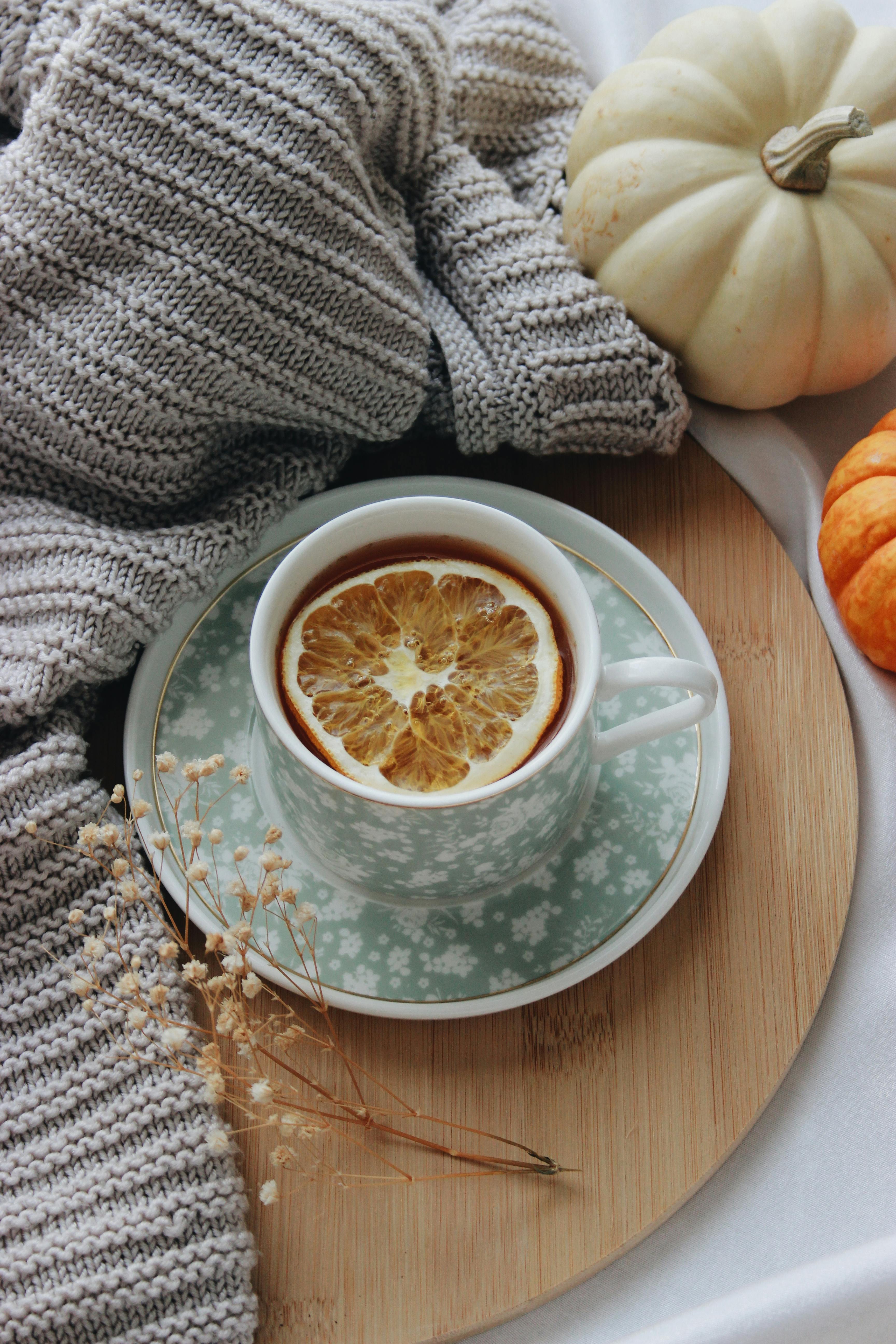 A warm autumn setting with tea, lemon, pumpkins, and knitwear. Ideal for fall vibes.
