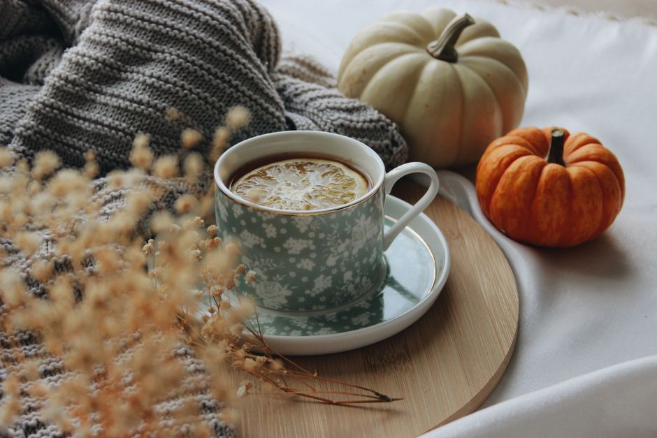 Warm autumn setting with a cup of tea, lemon slice, and decorative pumpkins on a wooden tray.