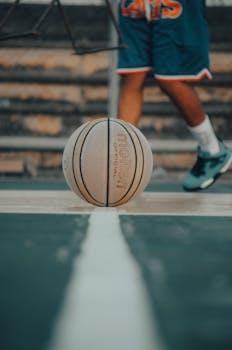 Focused basketball on court with player in background, emphasizing sports activity.