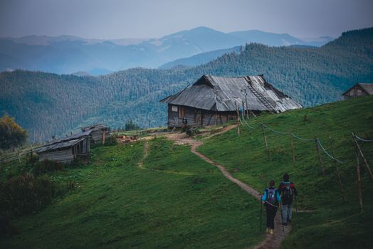 Two backpackers approach a rustic hut in the scenic Romanian mountains.