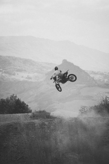 A black and white shot of a motocross rider performing an impressive jump in the scenic hills of Ravenna, Italy.