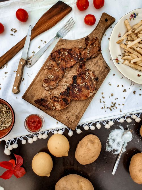 Free Top view of grilled meat with fries and tomatoes on a wooden board in a Greek setting. Stock Photo