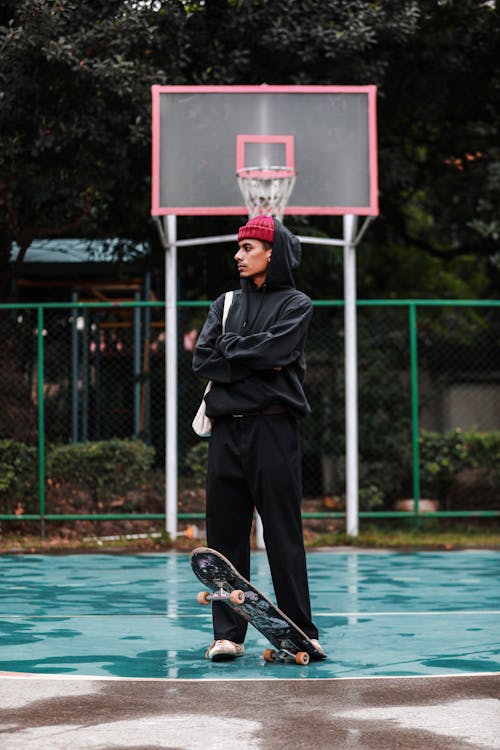 Man Standing with Skateboard on Basketball Court