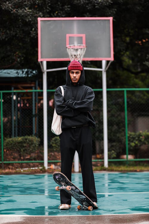 Man Standing with Skateboard on Basketball Court