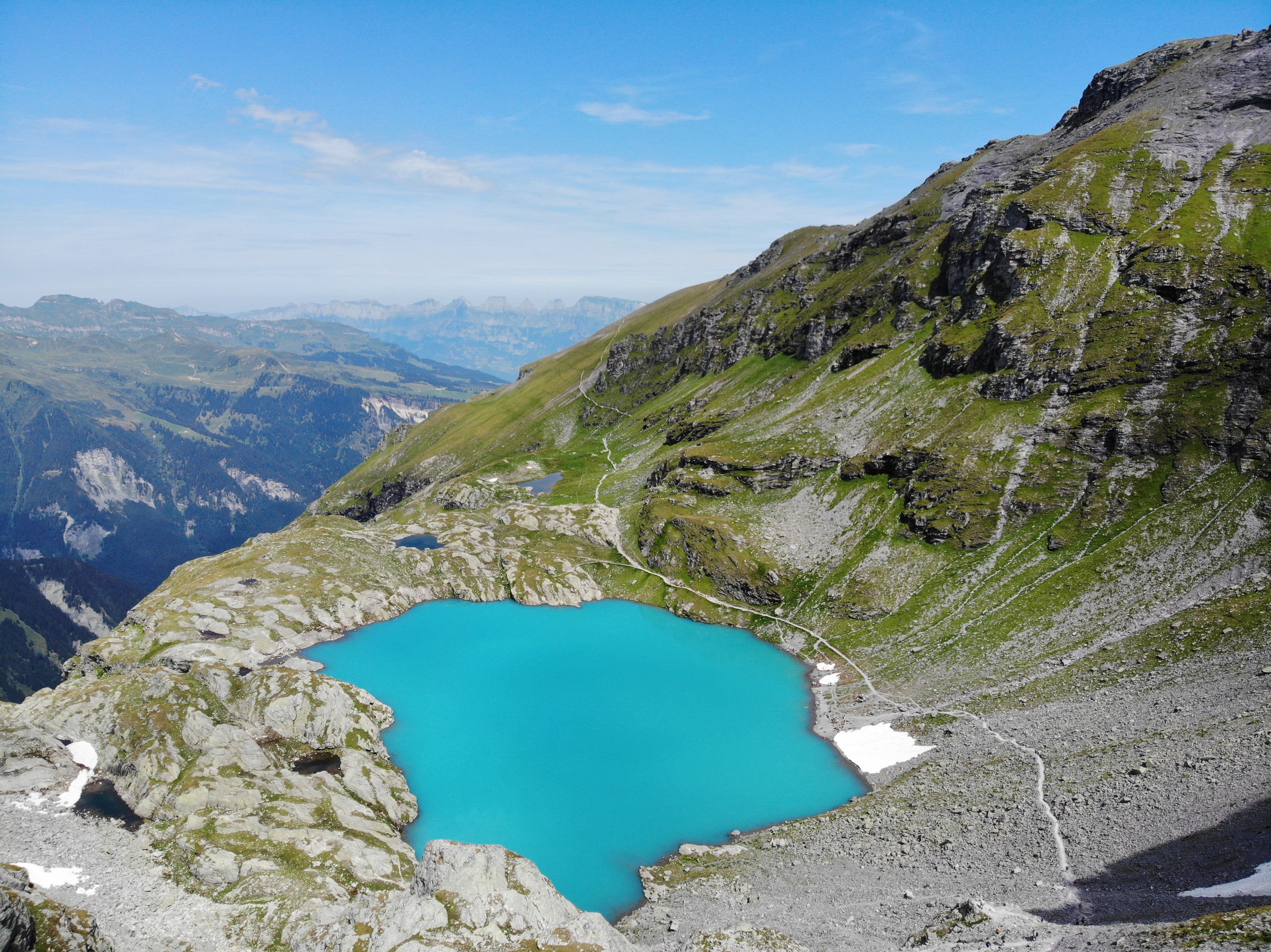 A stunning aerial view of a turquoise alpine lake surrounded by rugged Swiss mountains under a clear blue sky.