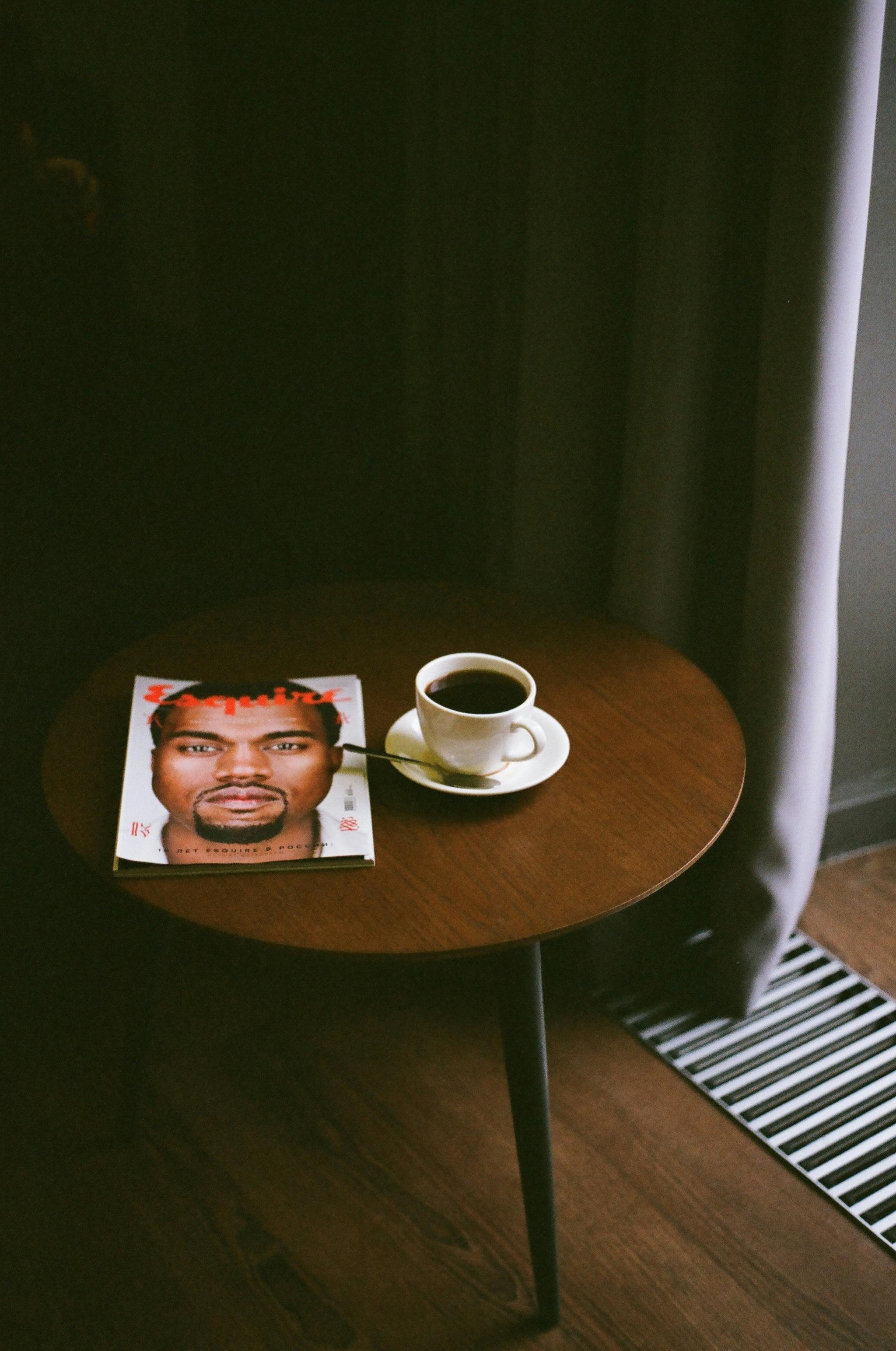 Free A relaxed and cozy setting with a cup of coffee and magazine on a round table by the window. Stock Photo