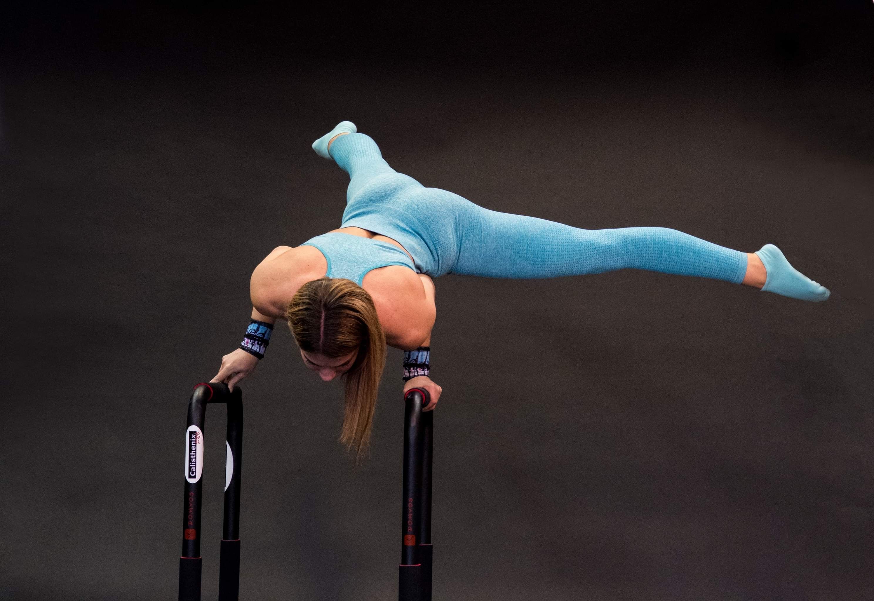 Athletic woman in blue activewear performing a handstand balancing move on parallel bars.