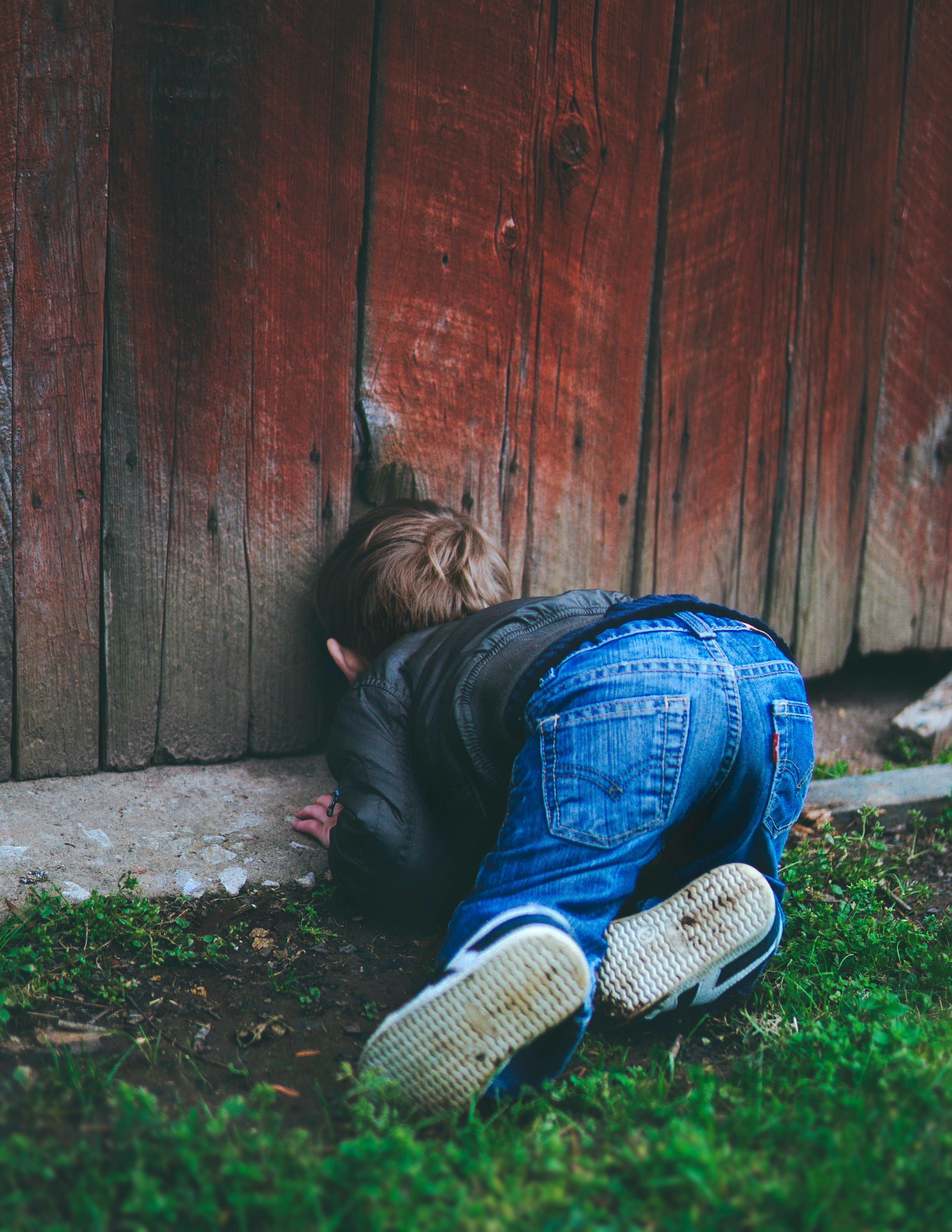 photo of boy peeking on brown wooden fence