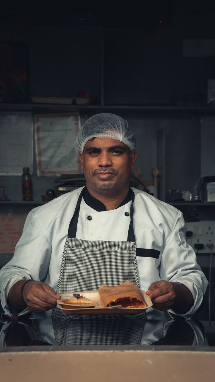 A Chef Holding A Plate Of Food While Looking At The Camera