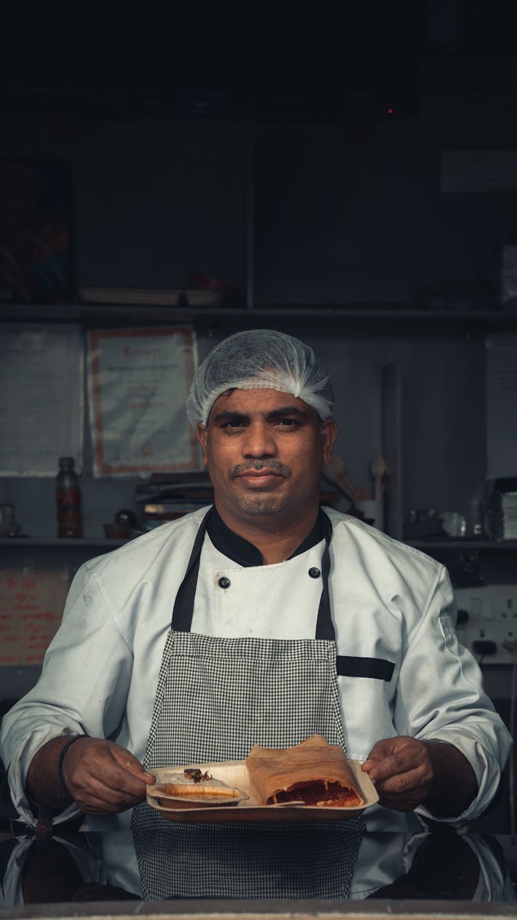 A Chef Holding A Plate Of Food While Looking At The Camera