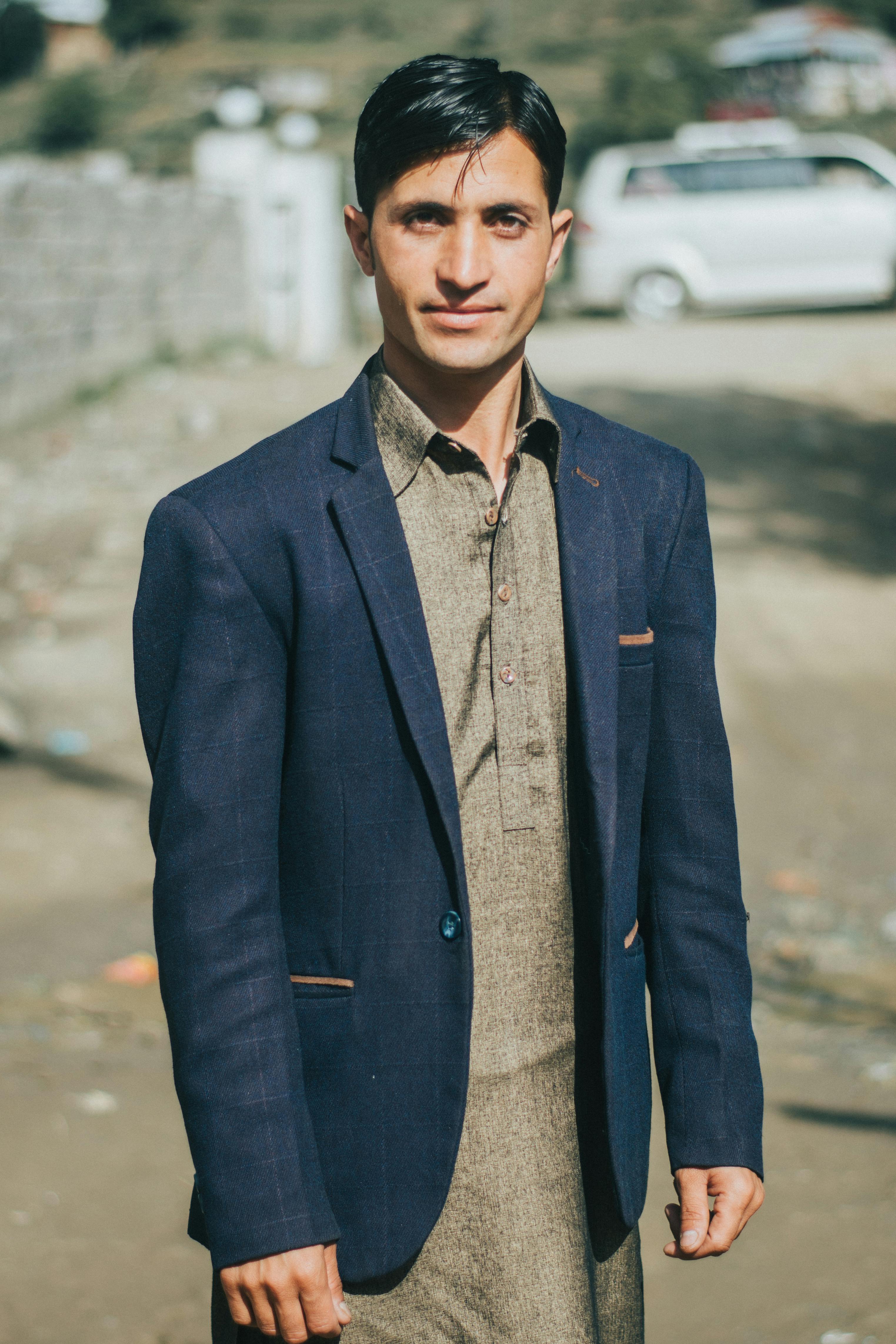 Portrait of a young man in formal attire standing outdoors on a sunny day.