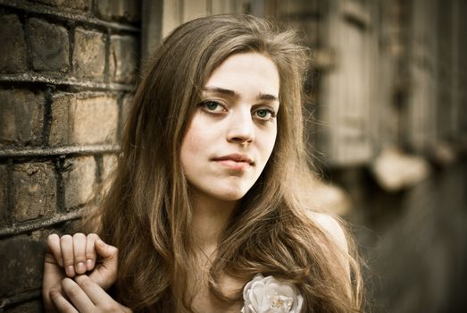 Beautiful portrait of a young woman leaning against a brick wall, exuding elegance and allure.
