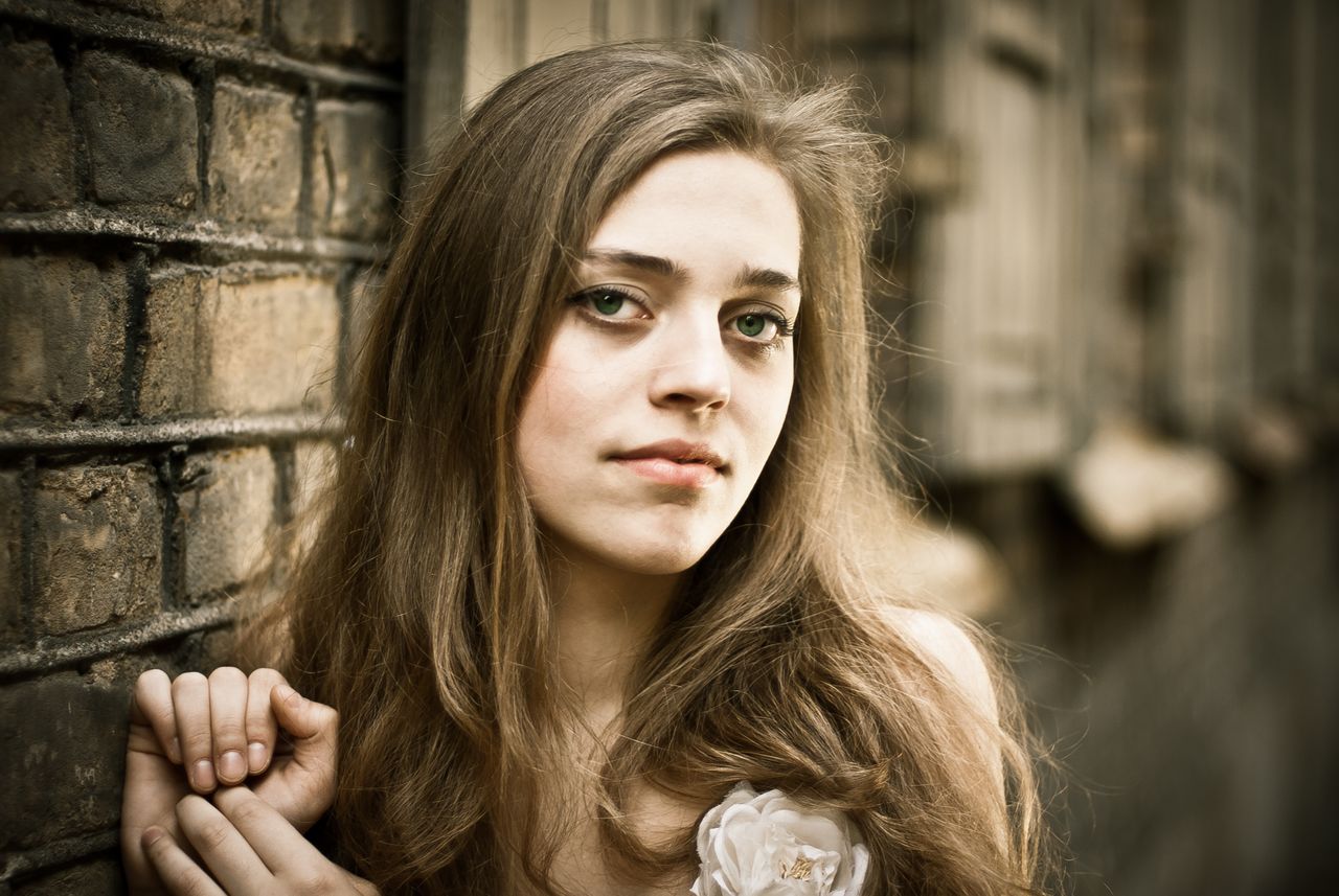 beautiful portrait of a young woman leaning against a brick wall exudi