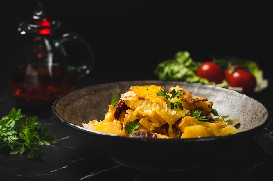 Close-up of a delicious pasta dish garnished with parsley and vegetables on a dark background. — Bacalhau à Gomes de Sá, a Portuguese dish.