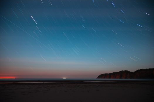 Long exposure captures star trails over a serene beach at night in Cloverdale, Oregon.