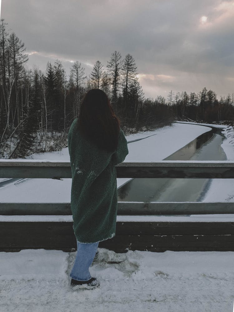 Woman Looking At Frozen River From Bridge