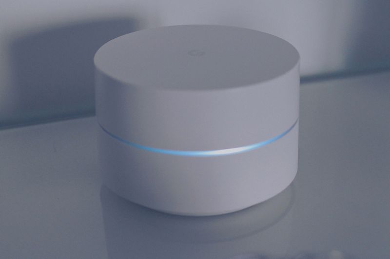A clean and modern minimalist design of a white round electronic device with a blue light ring on a reflective glass surface.