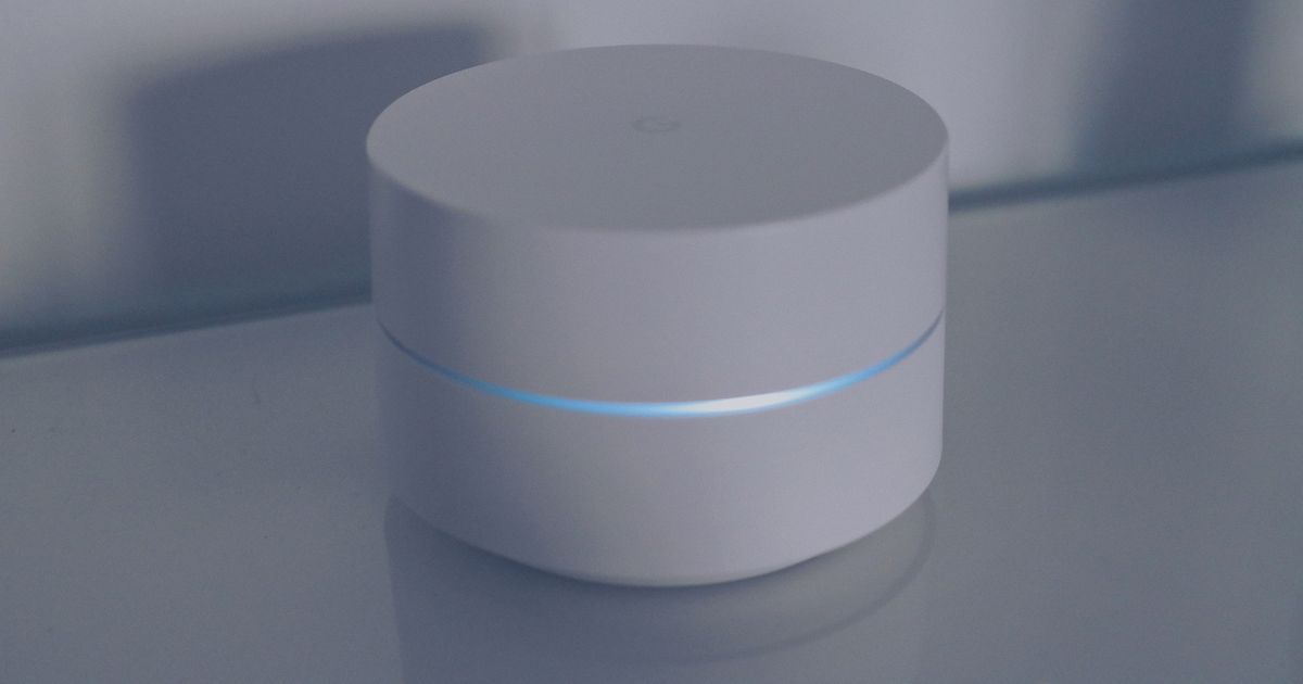 White round mesh Wi-Fi unit with a glowing blue light ring on a pale grey surface