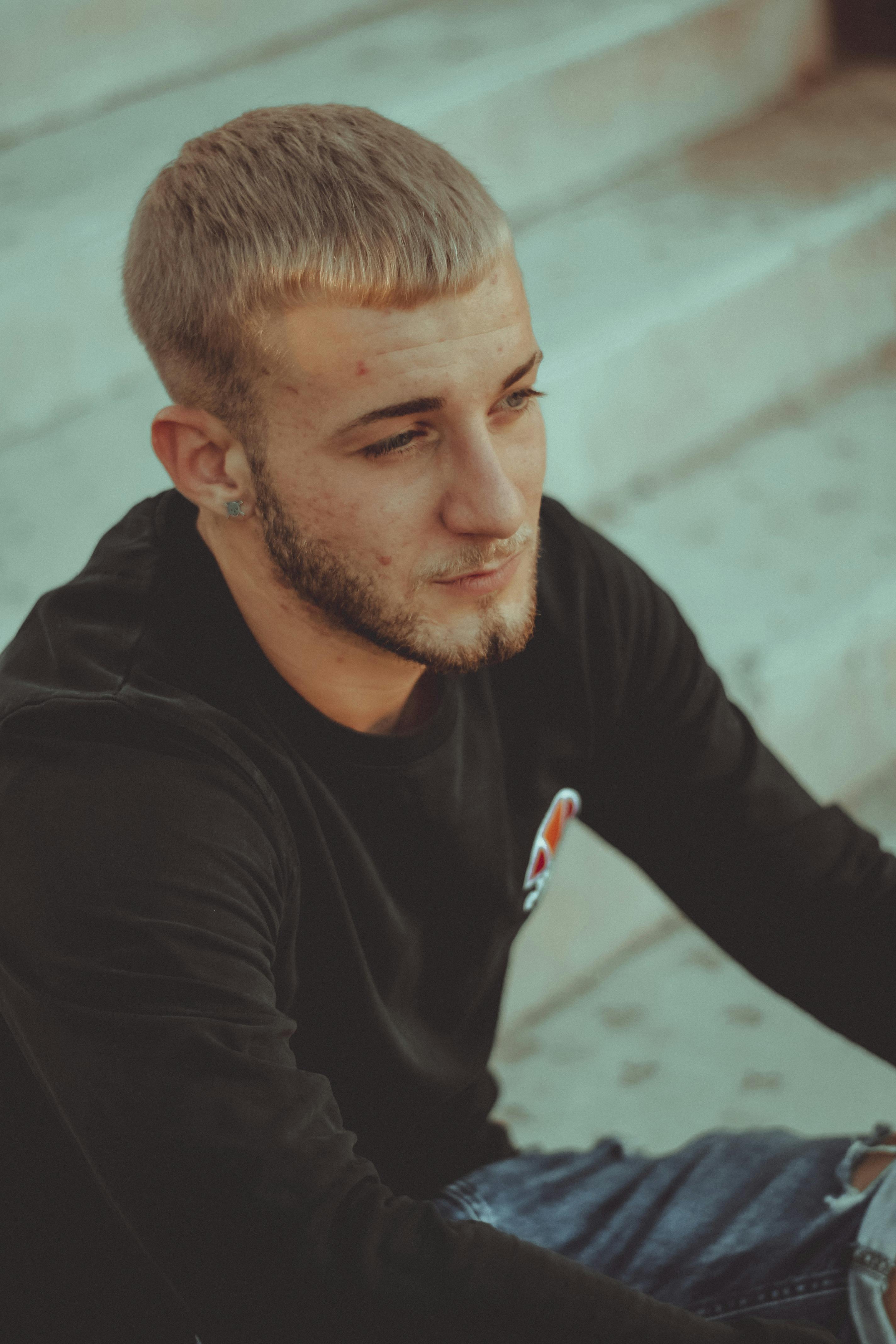 Young man in black attire sitting on concrete steps, deep in thought.
